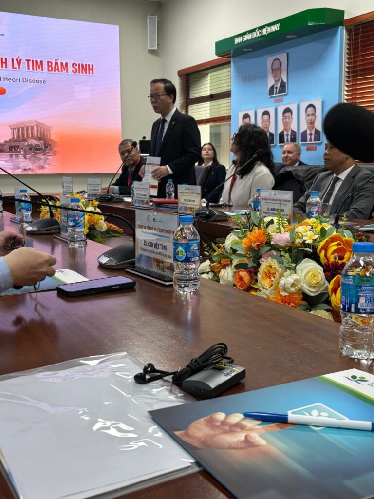 Man stands at conference table speaking while others look on.