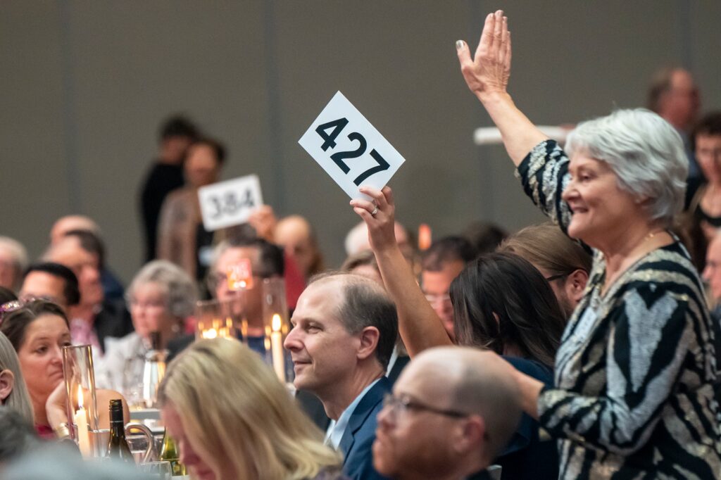 Bidder numbers held up in the air amongst seated guests.