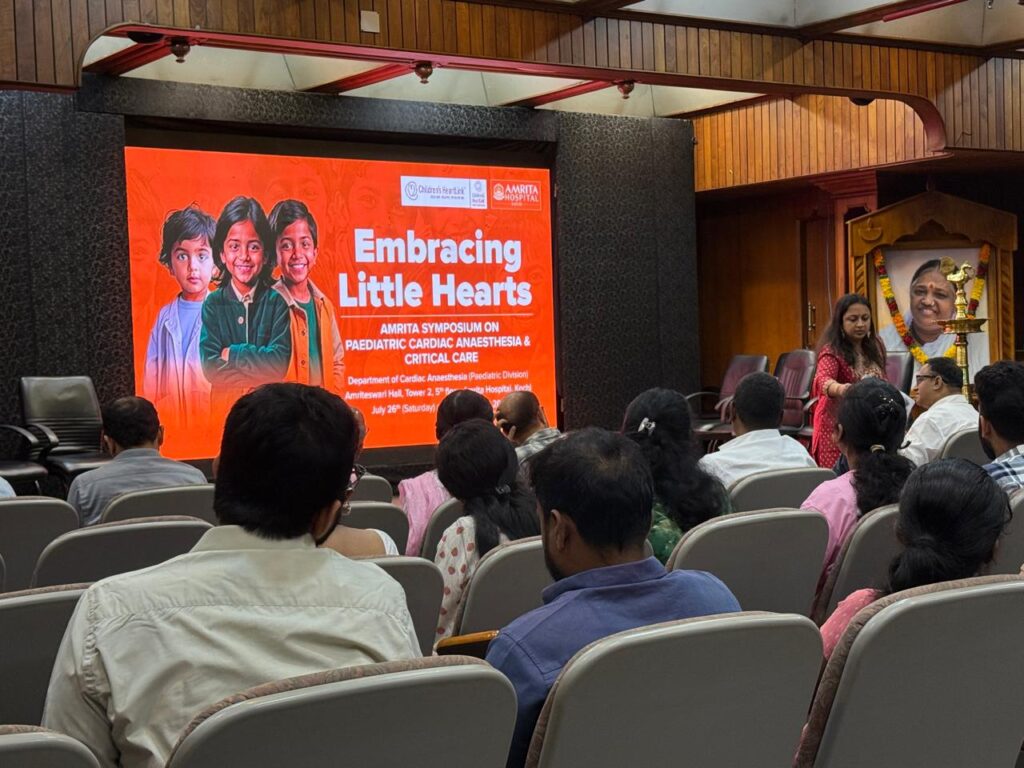 Auditorium full of people with large presentation screen on stage.