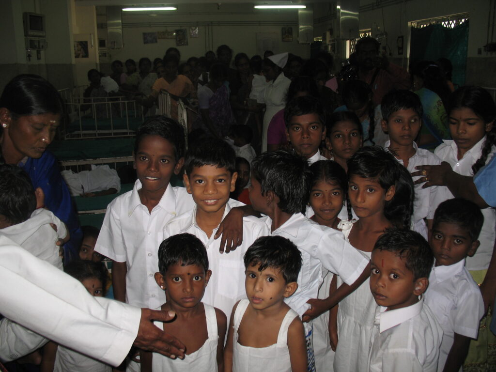 Kids in a crowded line inside a dimly lit hospital ward.