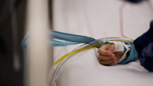 Close up of a small child's hand resting on a hospital bed with tubs running into it.