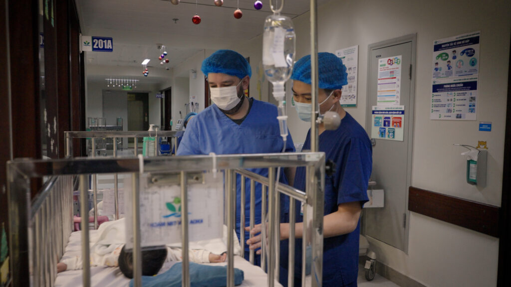 Two nurses checking on infant lying in a hospital crib.