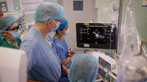 Medical professionals gathered around monitor with heart during surgery operation.